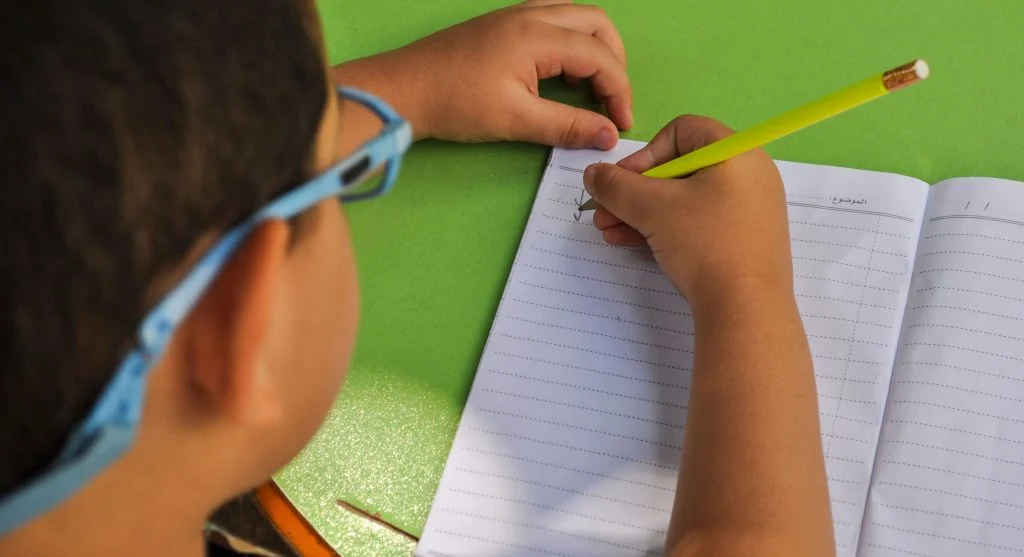 Child writing a sentence after first saying it aloud during home practice