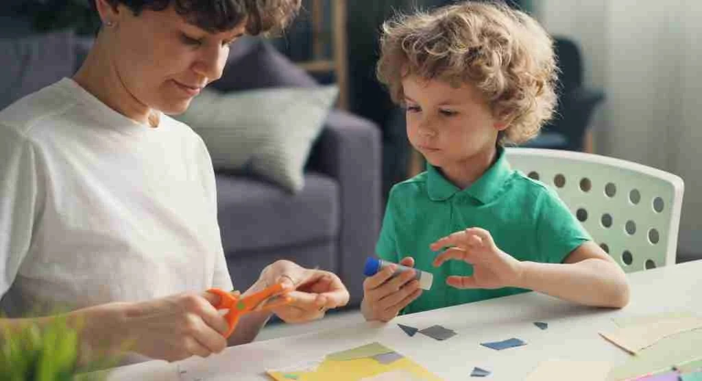Parent helping a child rotate paper during scissor practice at home