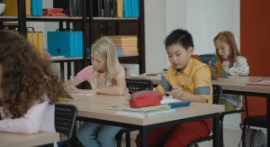 Child repeating homework directions while touching the first item on a study table