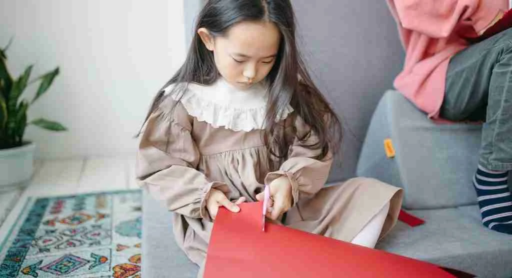 Child learning to guide paper while practicing cutting with scissors at home