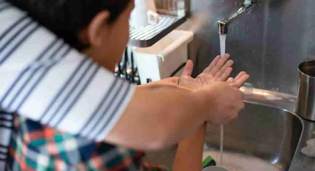 Parent guiding a child through hand washing with a towel prepared nearby